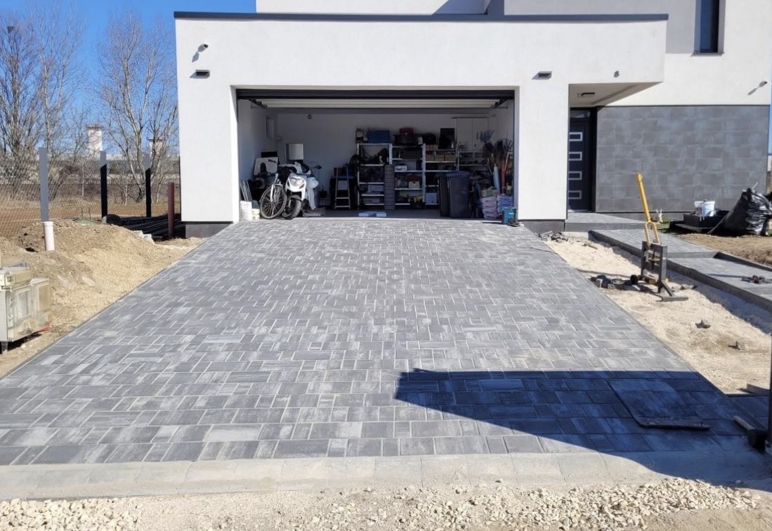 Allée en pavés autobloquants gris nuancés devant le garage double d'une maison contemporaine blanche, bordure de rive en limite